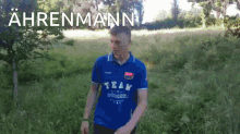 a man in a blue shirt with the word team on it is standing in a field