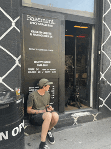 a man sits in front of a sign that says basement spicy snack bar