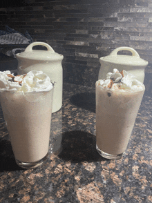 two glasses of milkshakes with whipped cream on top are on a counter