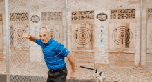 a man in a blue shirt is standing in front of a fence with a sign that says ' axe throwing '