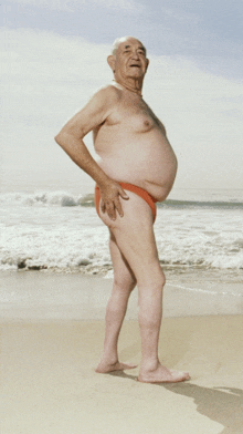 an elderly man in a red swim suit stands on the beach