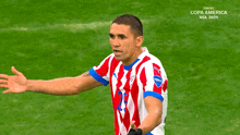 a man in a red white and blue striped shirt stands on a soccer field with the words copa america usa 2020 behind him