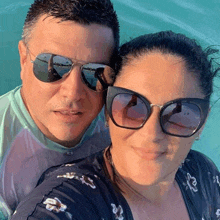 a man and a woman wearing sunglasses are posing for a selfie in the water .