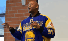 a man wearing a golden state warriors jersey stands in front of a brick wall