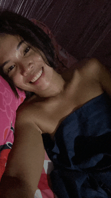 a woman wrapped in a blue blanket smiles while taking a selfie