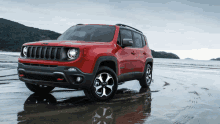 a red jeep is parked on a beach near the water