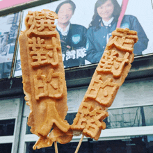 two sticks with chinese characters on them are sitting in front of a billboard