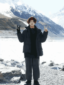 a man in a black jacket giving a peace sign in front of a mountain