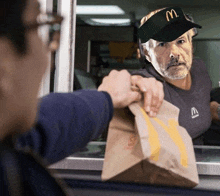 a man wearing a mcdonald 's hat holds a brown bag