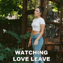 a woman in a white crop top and blue jeans is standing in front of a greenhouse with the words watching love leave