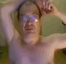 a shirtless man wearing glasses is making a funny face while holding his head .