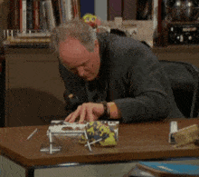 a man in a suit and tie is sitting at a desk with a book and scissors in front of him .