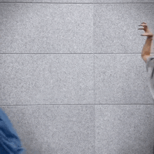 a man in a grey shirt is standing in front of a gray wall with his hands in the air