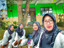 four women wearing hijabs and scarves pose for a picture in front of a green building