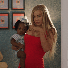 a woman in a red dress is holding a baby in front of a wall with a sign that says ice cream