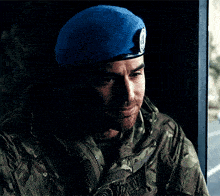 a man wearing a blue beret and a camouflage jacket looks at the camera