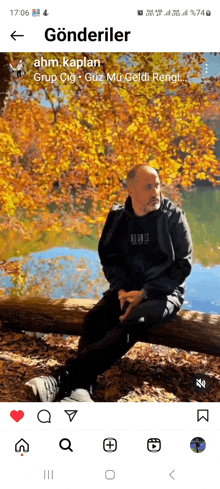 a man is sitting on a log in front of a lake with autumn leaves .