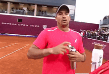 a man in a pink shirt is standing on a tennis court with the words srpska open 2023 behind him