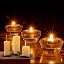 a group of lit candles in glass holders on a wooden table .