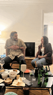 a man and a woman sit at a table with bottles of heineken on it