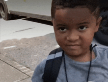 a young boy with a backpack is standing on the sidewalk looking at the camera