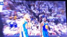 two basketball players are standing in front of a crowd on a tv screen .