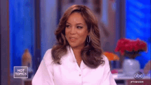 a woman is sitting on a stage wearing a white shirt and earrings on a television show .