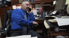 a man in a blue shirt and tie sits at a desk talking on a cell phone with 48 hours written on the bottom