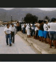 a group of people standing on the side of a road including a man wearing a shirt that says ave