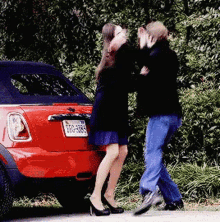 a man and woman are standing in front of a red mini cooper with a license plate that says 00-485