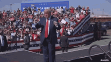 a man in a suit and tie is standing in front of a crowd with a sign that says america great again