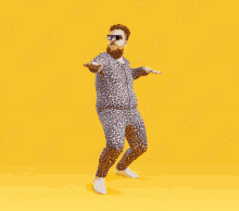 a bearded man wearing a leopard print outfit and sunglasses is dancing on a yellow background .