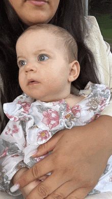 a woman is holding a baby in her arms and the baby is wearing a floral dress