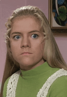 a girl with blonde hair and blue eyes is wearing a green turtleneck