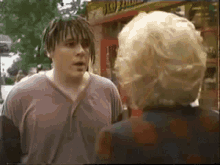 a man with dreadlocks is talking to a woman with blonde hair in front of a hot dog stand .