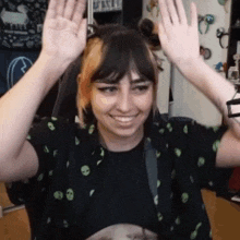 a woman is smiling and raising her hands in the air while wearing a black shirt with aliens on it .