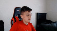 a young boy in a red shirt is sitting in an gtr gaming chair