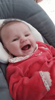 a baby in a red dress is laying in a bouncer and smiling .