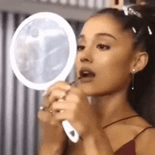 ariana grande is applying lipstick in front of a mirror in a room .