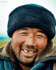 a man with a beard wearing a black hat and a blue jacket smiles for the camera