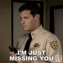 a man in a sheriff 's uniform is holding a cell phone and saying i 'm just missing you