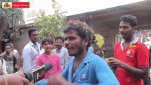 a man in a blue shirt is talking into a microphone in front of a group of people with a sign that says telugu movies