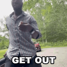 a man in a plaid shirt is dancing in front of a red car with the words get out written on it