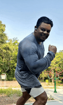 a man in a gray shirt and shorts is flexing his muscles in a park