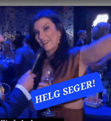 a woman in a brown dress is being interviewed by a man in a suit while holding a glass of wine