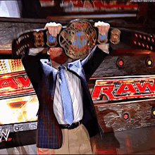 a man in a suit and tie holds a wrestling championship belt over his head in front of a raw sign