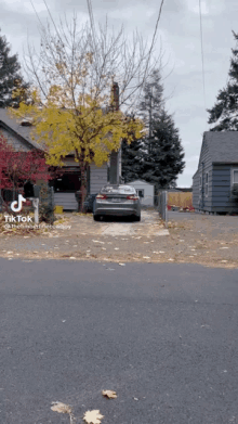 a car is parked in a driveway next to a house and a tree