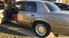 a silver car is parked in a driveway with the door open and a person sitting in the driver 's seat