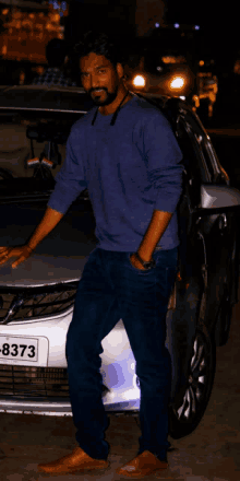 a man stands in front of a silver car with a license plate that says 8373