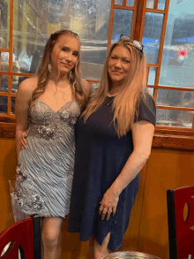 a woman in a blue dress stands next to a woman in a silver dress